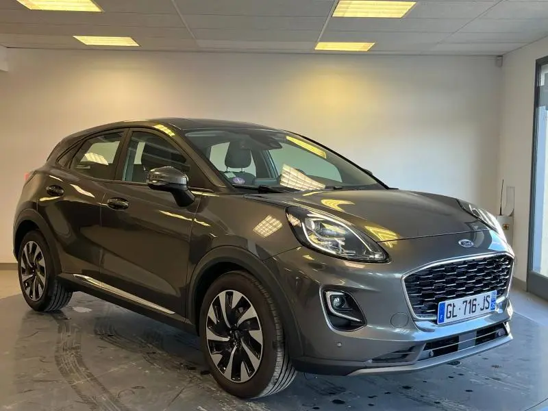 Vue 3/4 avant droit d'une Ford Puma 1.0 Flexifuel gris métallisé avec calandre imposante et jantes alu stylisées.
