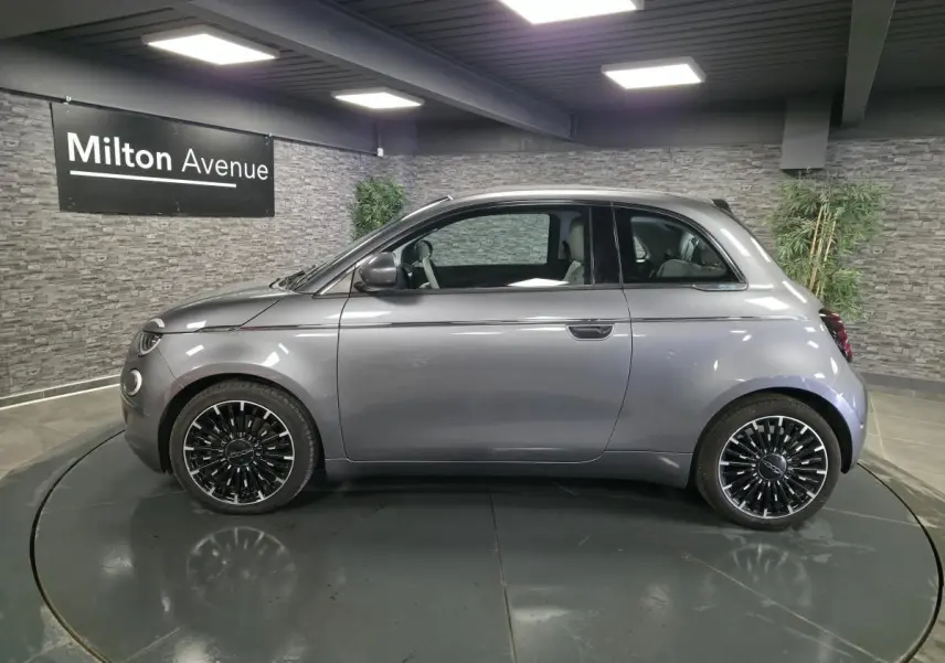 Profil droit d'une FIAT 500 Cabriolet électrique gris foncé avec jantes alliage bicolores en showroom.