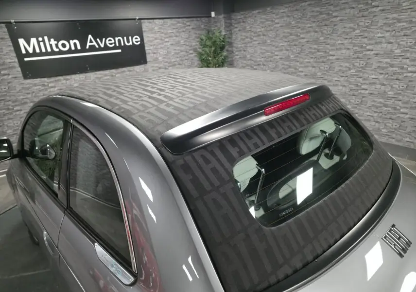 Vue arrière côté gauche d'une FIAT 500 Cabriolet électrique gris foncé avec capote à motif FIAT visible.