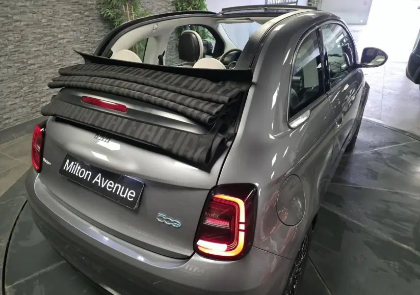 Vue 3/4 arrière droite d'une FIAT 500 Cabriolet électrique gris foncé avec capote partiellement ouverte et feux arrière allumés.