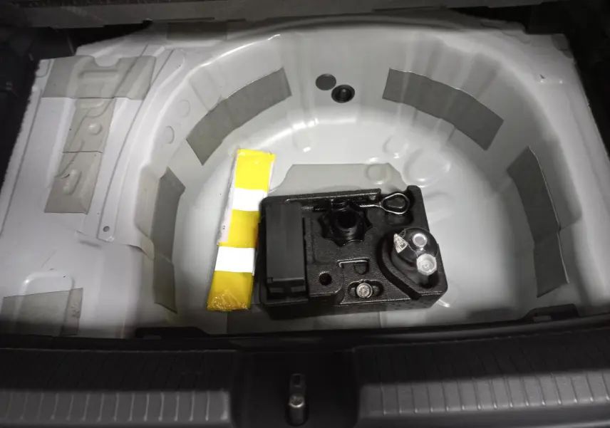 Coffre ouvert montrant le rangement sous plancher blanc avec kit de réparation et emplacement roue de secours.