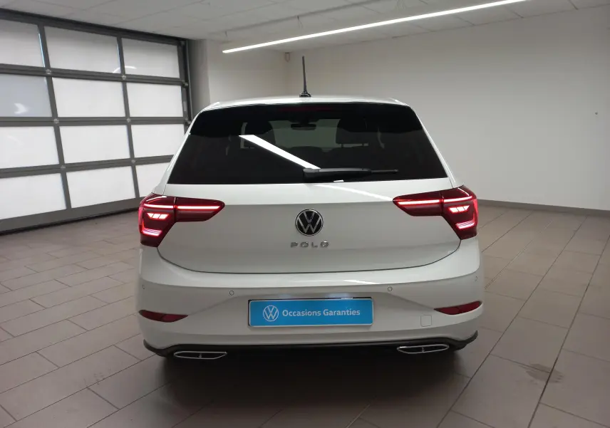 Vue arrière d'une Volkswagen Polo blanche avec feux allumés et vitres arrière surteintées dans un garage.