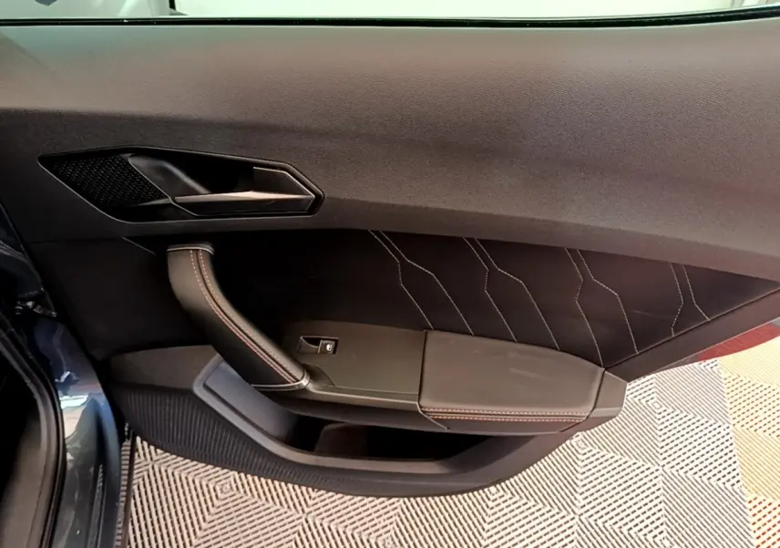 Gros plan sur la porte intérieure côté gauche du CUPRA Formentor gris foncé, avec surpiqûres rouges et poignée en cuir.