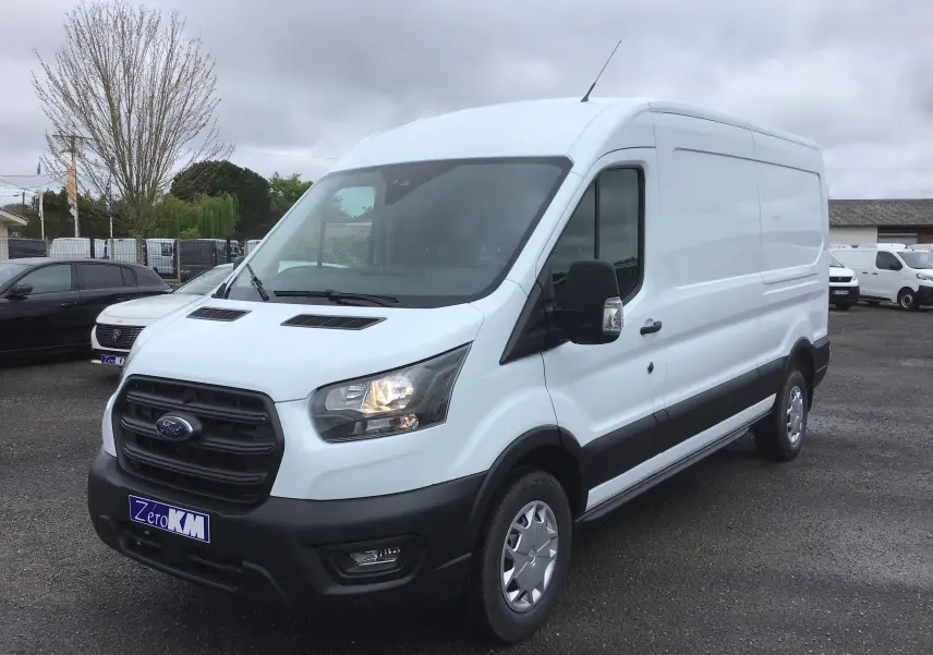 Fourgon Ford Transit blanc vu en 3/4 avant droit, avec calandre noire et feux allumés sur parking extérieur.