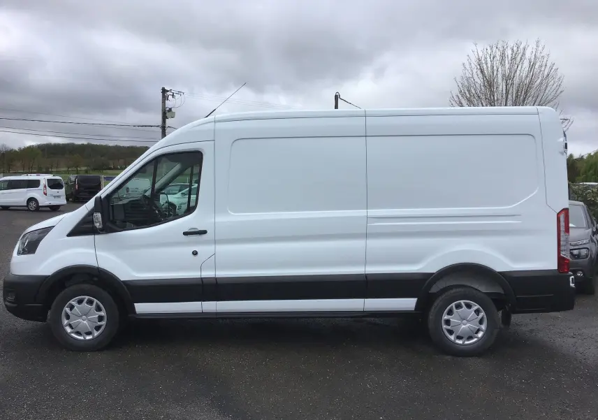 Vue de profil côté gauche d'un fourgon Ford Transit blanc 350 L3H2 avec bande noire basse sur un parking extérieur.