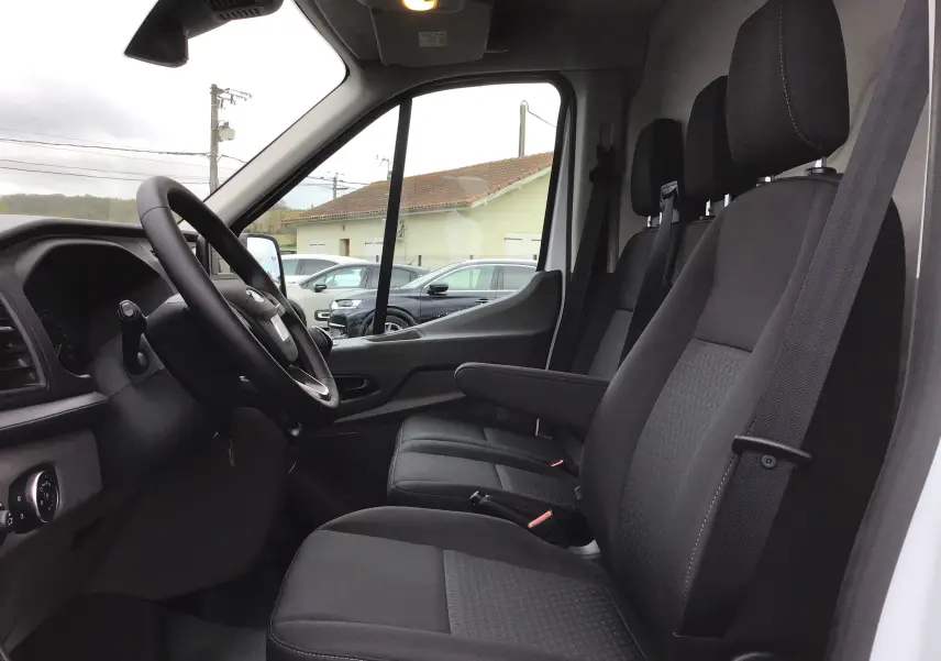 Vue intérieure côté conducteur du Ford Transit Fourgon blanc 2023, montrant les sièges noirs et le volant.