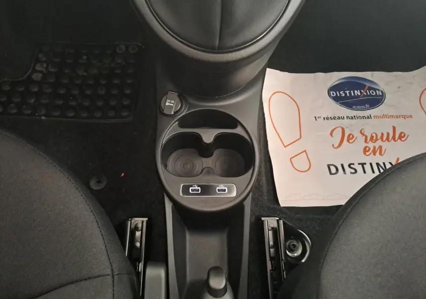 Vue plongeante sur la console centrale noire de la Fiat 500 blanche, avec porte-gobelets et prises USB visibles entre les sièges.