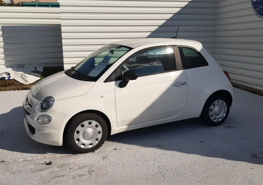 Vue de profil côté gauche d'une Fiat 500 blanche 3 portes garée devant un mur blanc en extérieur.