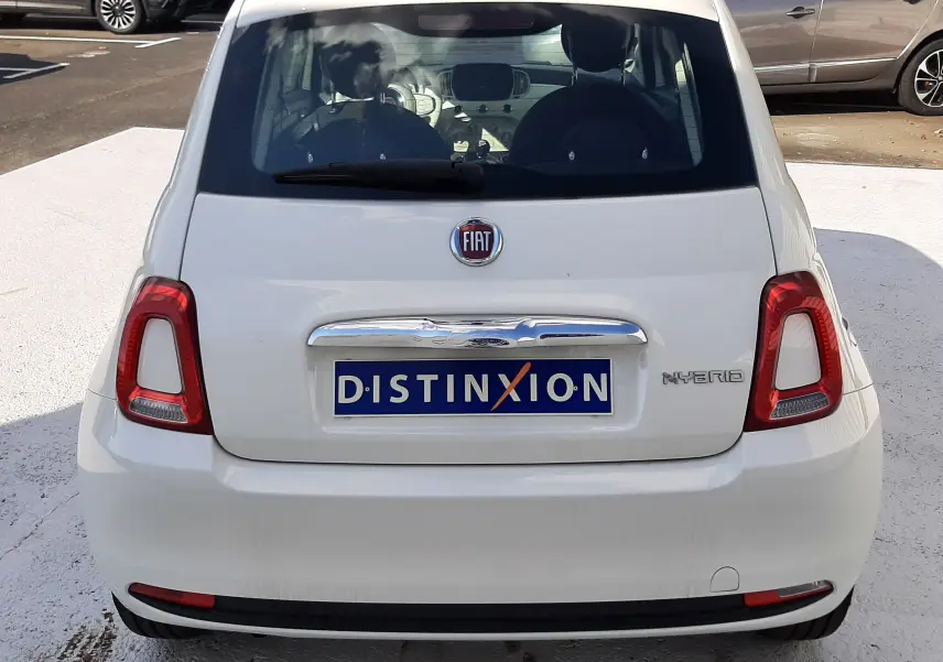 Vue arrière d'une FIAT 500 blanche hybride avec logo FIAT et badge Hybrid visible sur un parking.