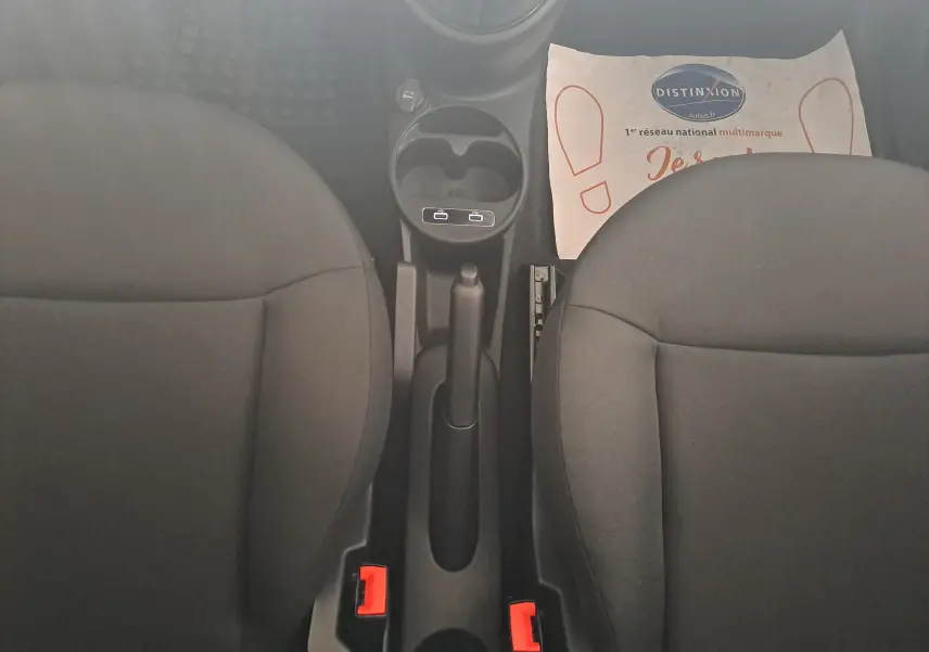 Vue plongeante sur la console centrale et les sièges noirs du Fiat 500 blanc, avec frein à main et porte-gobelets visibles.