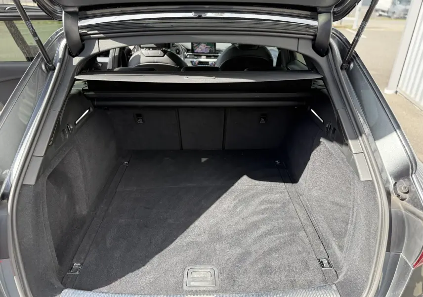 Coffre ouvert vu de l'arrière d'une Audi A4 Avant 35 TDI gris Daytona metal, intérieur noir et espace de chargement spacieux.