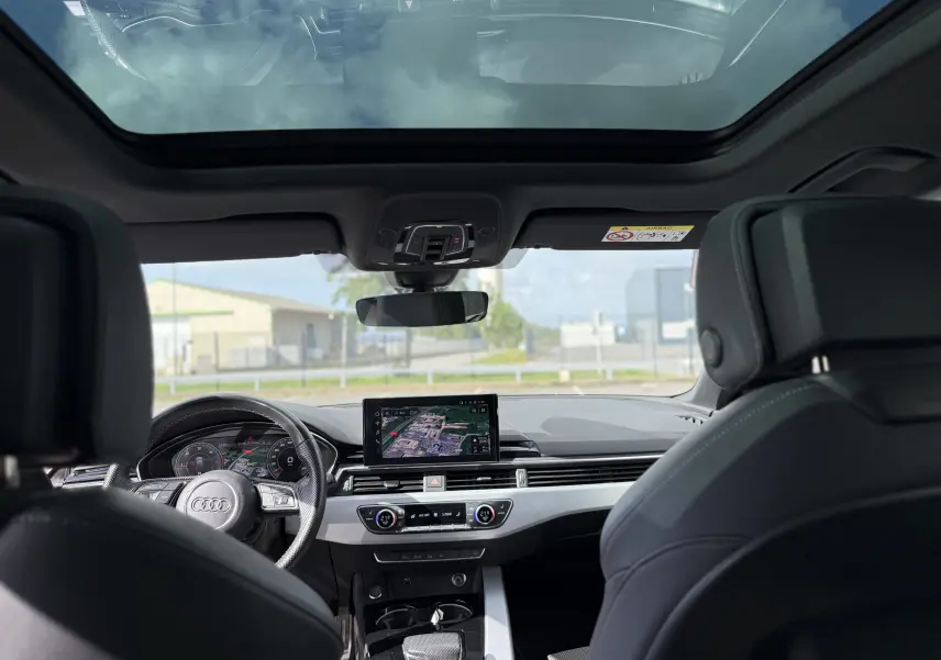 Vue intérieure avant de l'Audi A4 Avant gris Daytona, avec tableau de bord numérique et toit panoramique en verre.