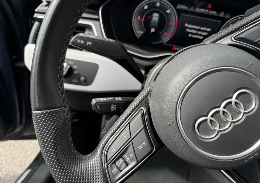 Gros plan sur le volant en cuir noir perforé et le tableau de bord numérique de l'Audi A4 Avant gris Daytona 2023.