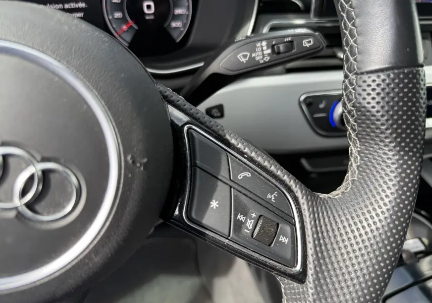 Gros plan sur la partie gauche du volant en cuir perforé de l'Audi A4 Avant gris Daytona, avec commandes audio intégrées.