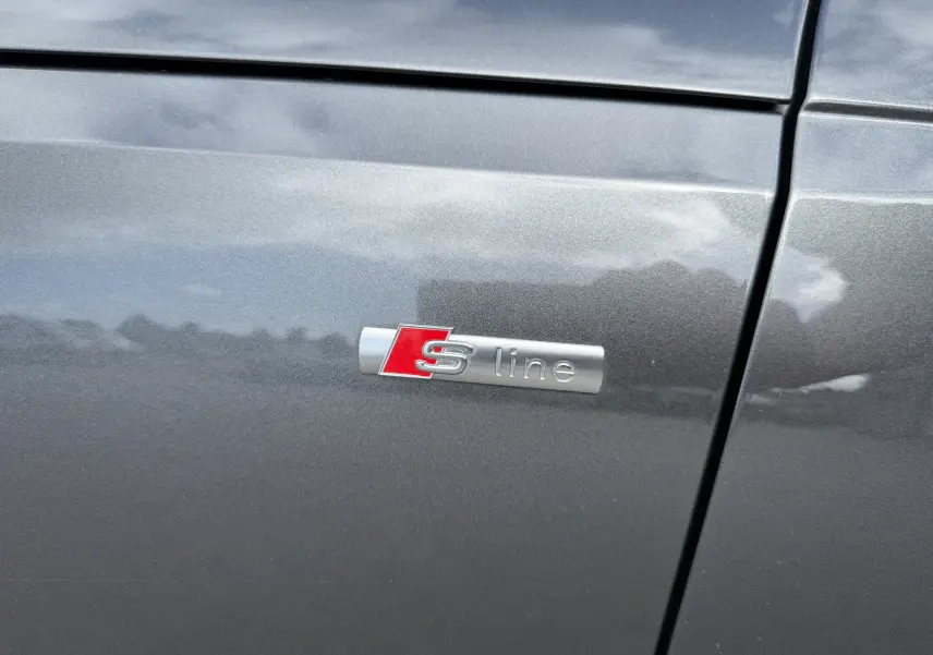 Gros plan sur l'écusson S line rouge et argent sur la porte gris Daytona métallisé d'une Audi A4 Avant 2023.