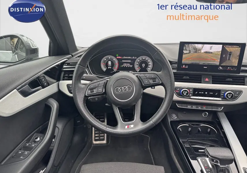 Intérieur de l'Audi A4 Avant 35 TDI 2023, vue du poste de conduite avec volant S-Line et écran multimédia allumé.