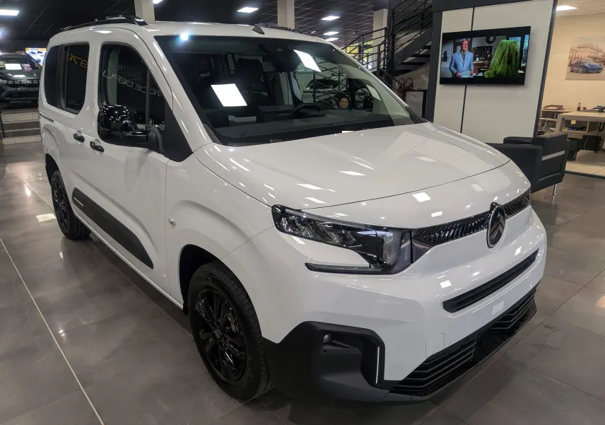 Vue 3/4 avant gauche d'un Citroën Berlingo blanc Glacier avec jantes noires et détails noirs contrastants en intérieur showroom.