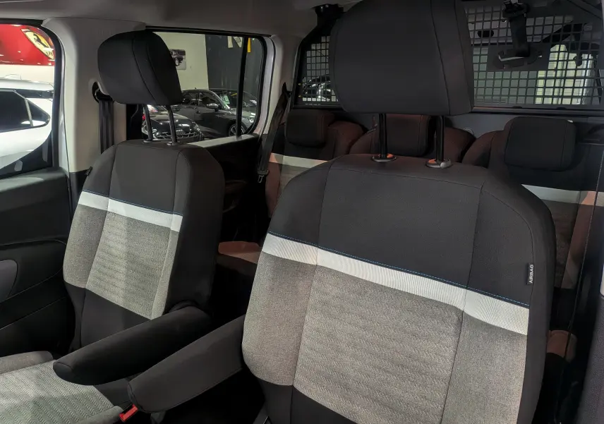 Gros plan sur les sièges avant en tissu gris et noir du Citroën Berlingo Blanc Glacier, version utilitaire avec séparation grillagée.
