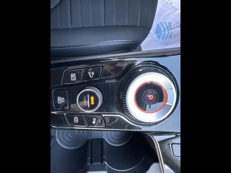Vue rapprochée de la console centrale noire brillante du Kia Sportage 2022 avec sélecteur de mode de conduite et bouton de frein à main électronique.