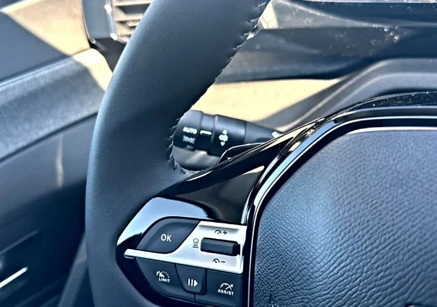 Gros plan sur le volant cuir noir de la Peugeot 408 Hybrid 145 allure, avec commandes intégrées côté gauche.