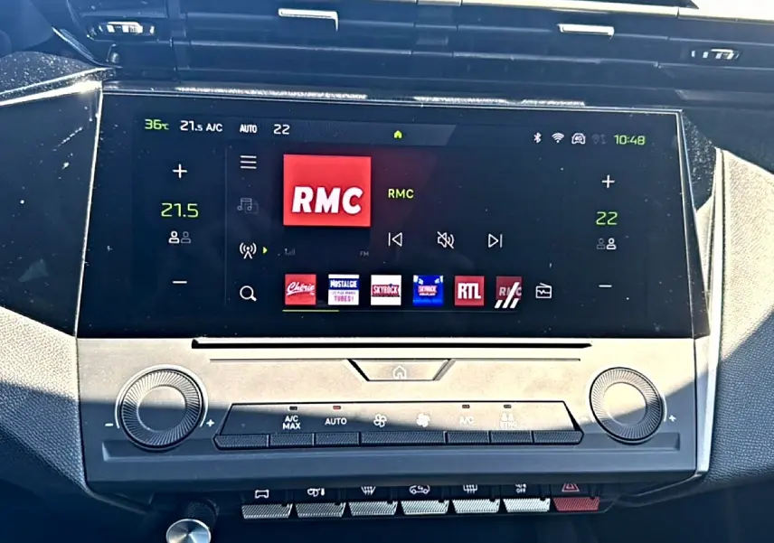 Écran tactile central du tableau de bord du Peugeot 408 Hybrid noir, affichant la radio RMC et commandes climatisation.