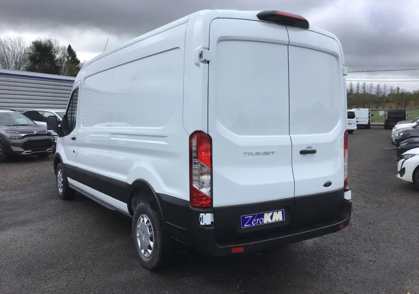 Vue 3/4 arrière droite d'un fourgon Ford Transit blanc avec portes arrière fermées sur un parking.