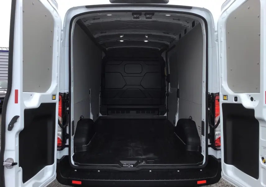 Vue arrière du fourgon blanc Ford Transit 350 L3H2 2023, portes ouvertes montrant l'espace de chargement vide et éclairé.