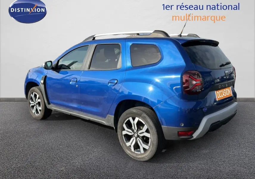 Vue 3/4 arrière droite d'un Dacia Duster bleu Iron 2022 avec jantes alliage et toit noir contrasté.