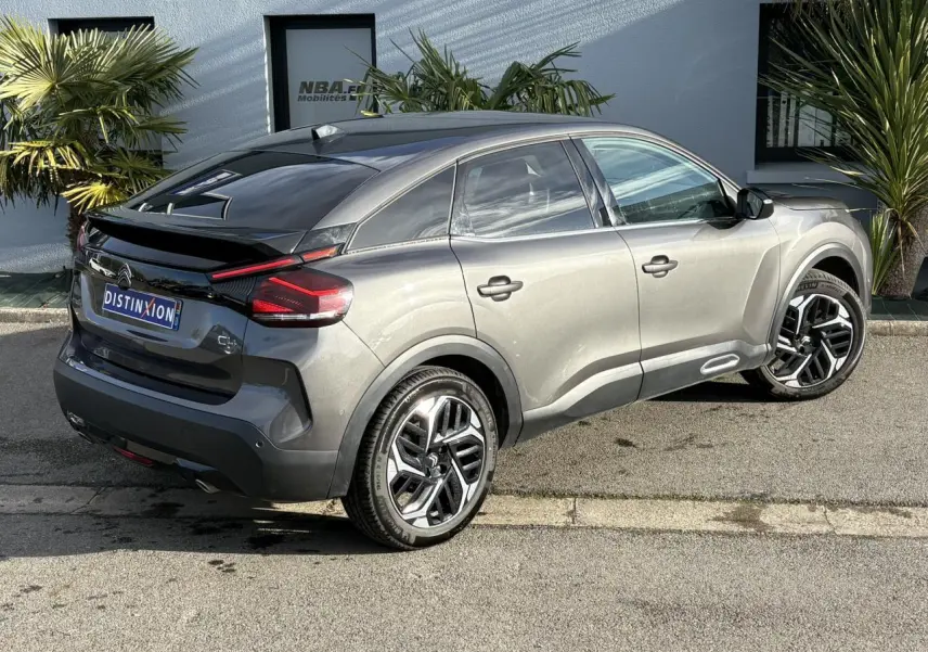 Vue 3/4 arrière droite d'une Citroën C4 2024 gris Platinium avec jantes alliage 18'' et toit noir brillant.