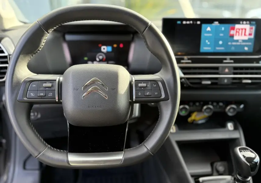 Vue intérieure centrée sur le volant cuir noir de la Citroën C4 2024 avec écran tactile et levier de vitesse manuel.