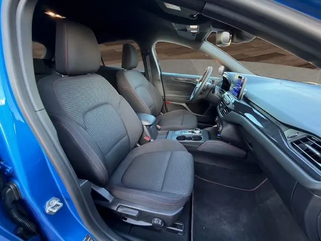 Vue intérieure côté conducteur de la Ford Focus 1.5 EcoBoost ST-Line 2022 bleu, sièges noirs avec surpiqûres rouges et tableau de bord moderne.
