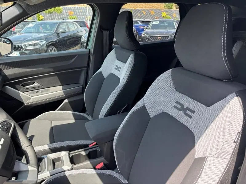 Vue intérieure des sièges avant gris clair et foncé du Dacia Bigster 2025 avec accoudoir central et logo brodé.