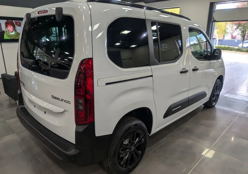 Vue 3/4 arrière droite du Citroën Berlingo blanc Glacier avec vitres teintées et jantes noires en showroom.