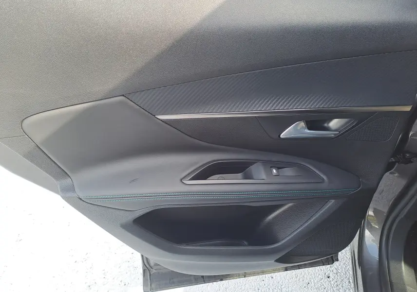Porte intérieure côté gauche du Peugeot 3008 Hybrid gris platinium, avec poignée argentée et surpiqûres bleues.