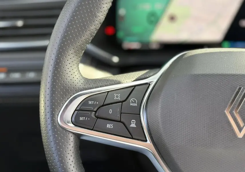 Gros plan sur les commandes au volant gauche du Renault Symbioz gris Cassiopée, avec boutons de régulateur et assistance.