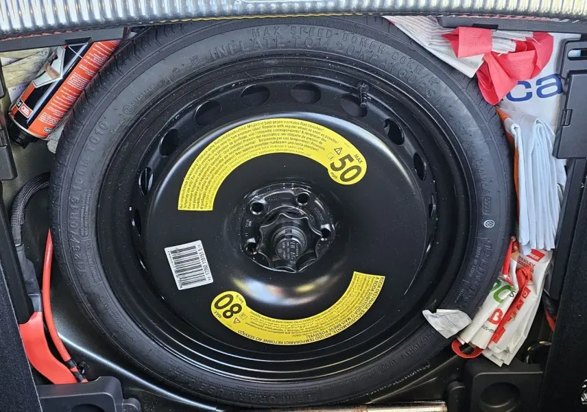 Roue de secours noire avec étiquettes jaunes visible dans le coffre d’une Audi A5 Sportback gris Daytona.