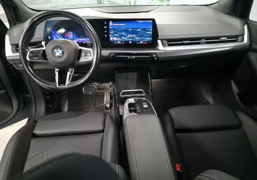 Intérieur noir de la BMW Série 2 218i Active Tourer 2023, vue du tableau de bord avec écran tactile incurvé et volant M cuir.