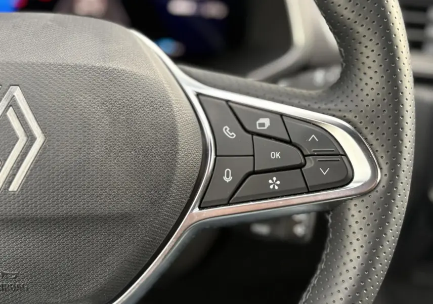 Gros plan sur le côté droit du volant perforé noir de la Renault SYMBIOZ avec commandes multifonctions intégrées.