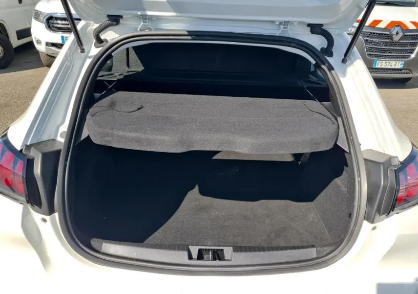 Coffre ouvert vu de l'arrière d'une Peugeot 208 Affaire blanche, montrant la plage arrière et l'espace de chargement vide.