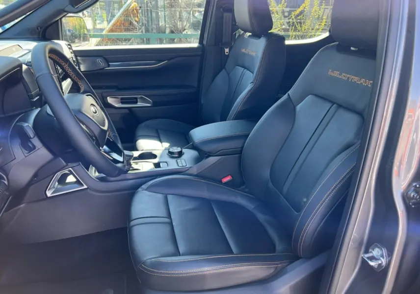 Intérieur côté conducteur du Ford Ranger 2025 gris carbone, sièges cuir Wildtrak avec surpiqûres orange et tableau de bord moderne.