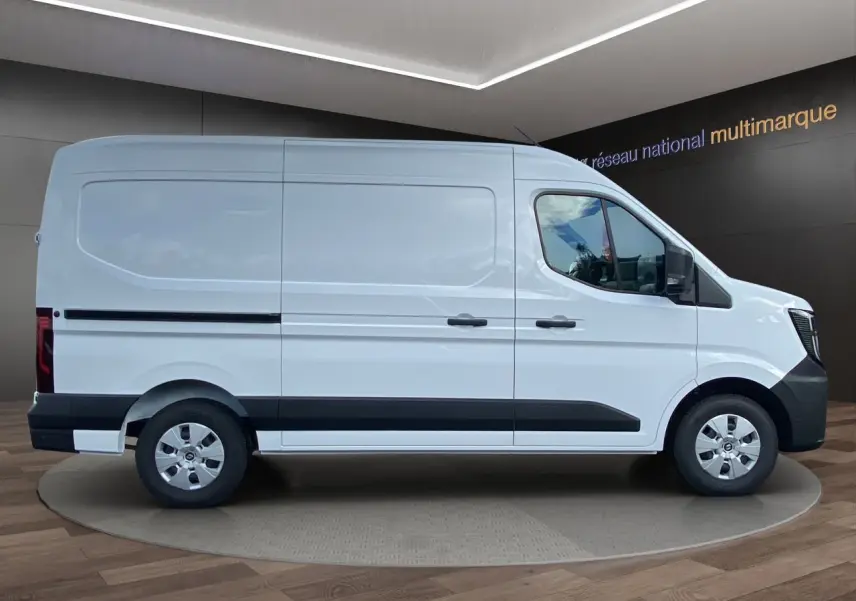 Vue de profil côté droit du Renault Master blanc 2025 avec bande noire et jantes argentées, dans un showroom intérieur.