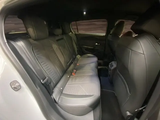 Vue intérieure arrière côté gauche de la Peugeot 308 hybride blanche, montrant les sièges en cuir noir et les détails de l'habitacle.
