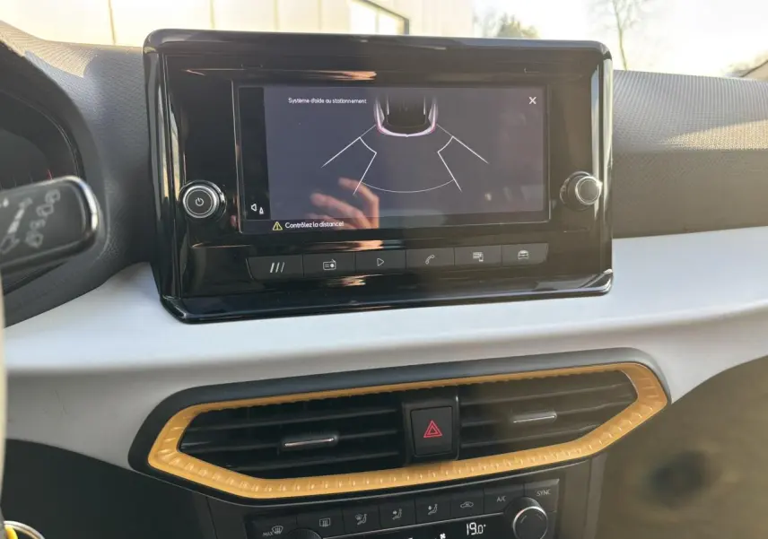 Vue rapprochée de l'écran tactile central affichant l'aide au stationnement dans l'habitacle clair du SEAT Arona blanc.