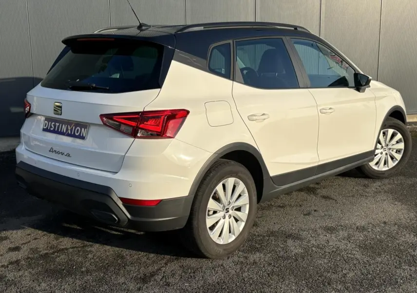 Vue 3/4 arrière droite d'un SEAT Arona blanc avec toit noir et jantes alliage 16 pouces, stationné sur sol goudronné.