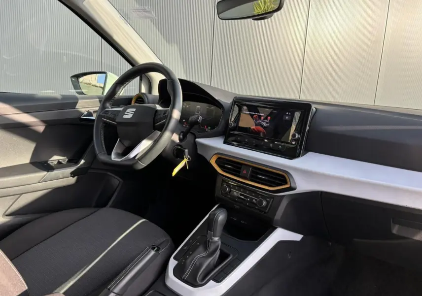 Vue intérieure côté conducteur du SEAT Arona blanc 2025, avec tableau de bord moderne et écran tactile central.