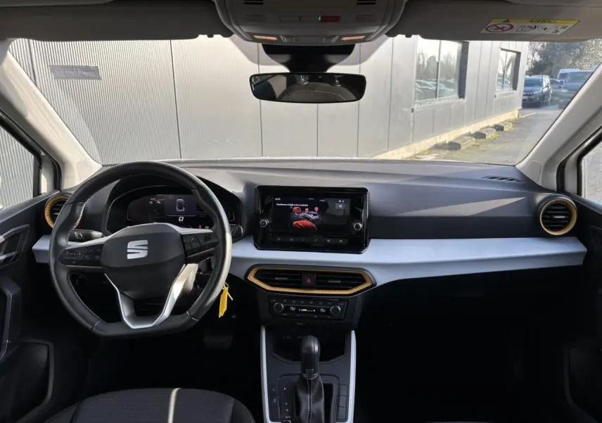 Vue intérieure avant du tableau de bord du SEAT Arona blanc, avec volant multifonction et écran tactile central.