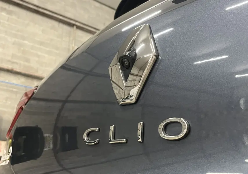 Gros plan sur le logo Renault et l’inscription Clio à l’arrière d’une Renault Clio V gris titanium dans un garage.