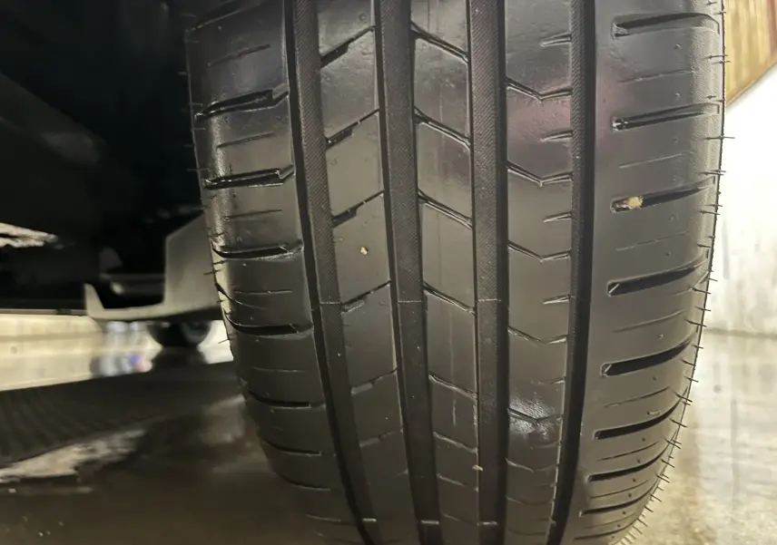 Gros plan sur le pneu avant droit d'une Renault Clio V gris titanium, montrant la bande de roulement et le dessous du véhicule.