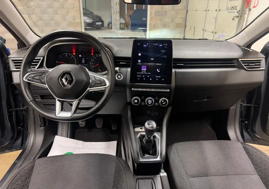 Vue intérieure avant de la Renault Clio V Business 2019, avec tableau de bord noir, écran tactile vertical et levier de vitesses manuel.