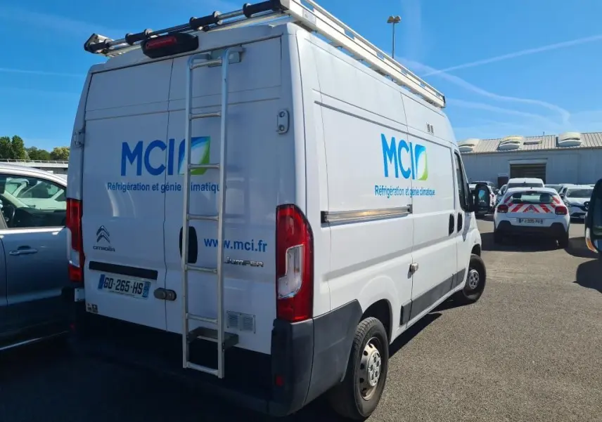Vue 3/4 arrière droite d’un Citroën Jumper blanc avec galerie, échelle et logo MCI sur la carrosserie.